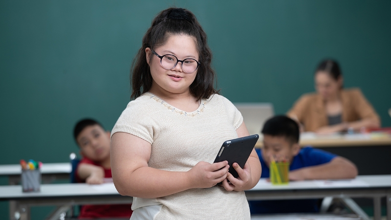 Photo of a young woman with Down Syndrome smiling and carrying schoolbooks
