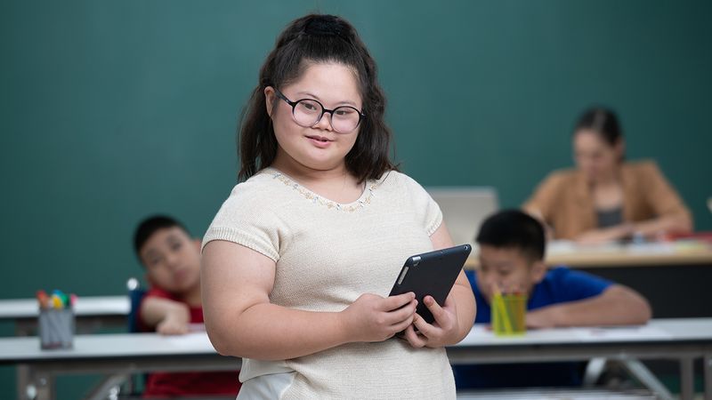 Photo of a young woman with Down Syndrome smiling and carrying a tablet