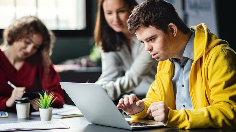 Photo of a student using technology alongside another student and an adult